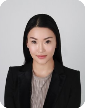 Portrait of a woman with long black hair, wearing a black blazer and a light-colored blouse against a plain background.