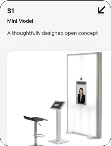 A minimalist open-concept booth with a small seating stool, a touchscreen kiosk, and a tall white frame with a mounted screen showing a woman, labeled 'S1 Mini Model'.