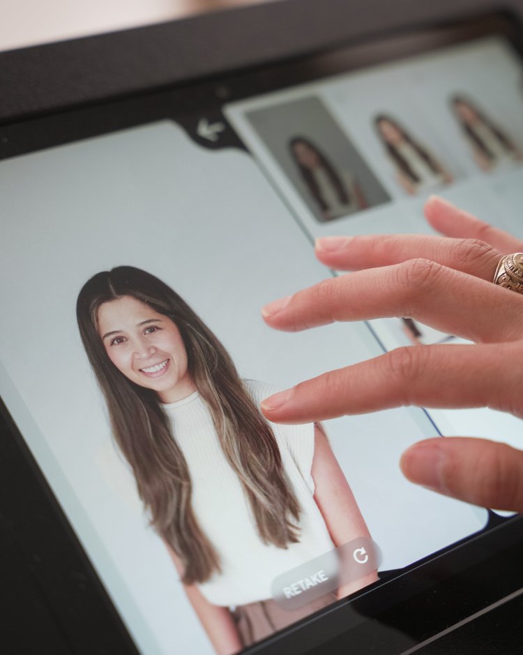Close-up of a hand with a ring touching a photo on a tablet screen of a woman with long brown hair smiling at the camera, with smaller thumbnail images of the same woman in the background.