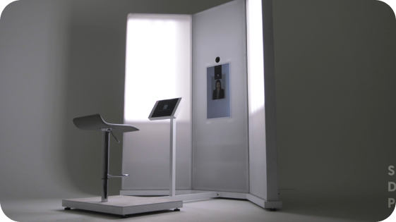 A sleek photo booth with a digital screen and a stool, set against a white backdrop.