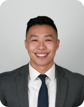 Portrait of a smiling young Asian man wearing a gray suit, white shirt, and dark tie against a plain background.