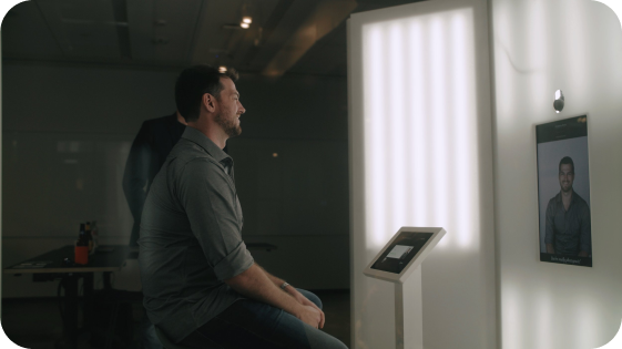 Man sitting and watching a video call on a wall-mounted screen in a modern office or conference room.